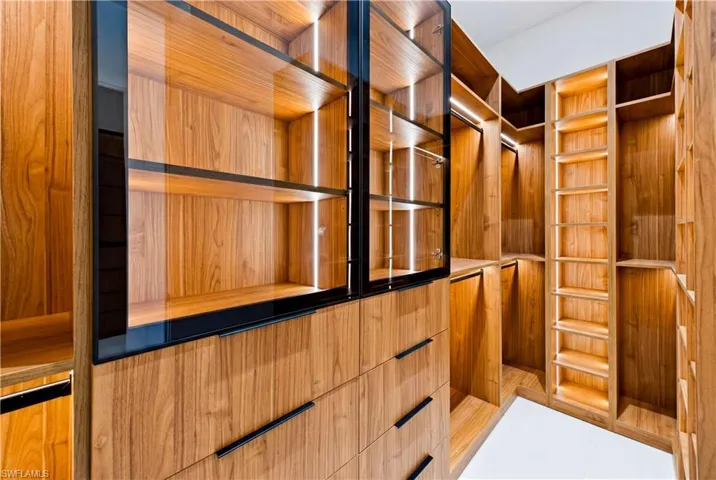 Boutique-style custom closet with illuminated display cabinetry, extensive shelving, and organized space for wardrobe, shoes, handbags, and accessories