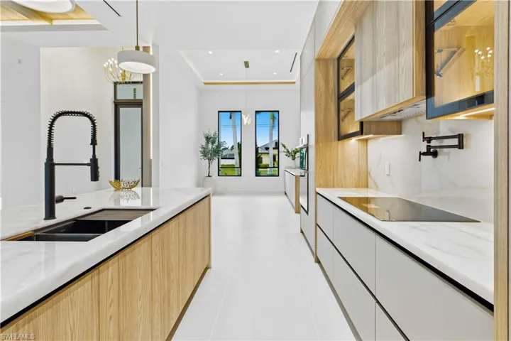 OVERSIZED Cristallo quartzite waterfall island w/ sculptural angled ends, elegant white & gold pendant lighting & CABINETRY w/ under- & upper-cabinet lighting, QUARTZITE COUNTERTOPS, full-height backsplash, POT FILLER & large sink