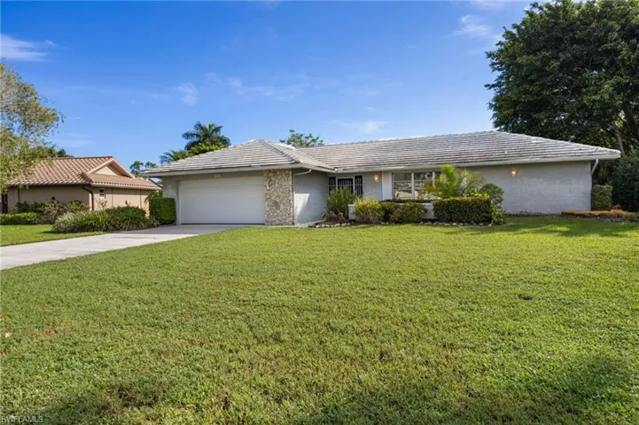 Stucco exterior with stone accents, a tile roof, an attached garage, a concrete driveway, and established landscaping