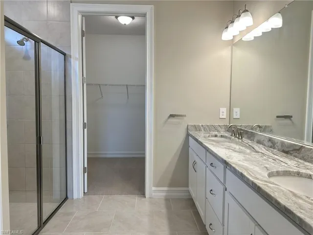 Full bath with a stall shower, double vanity, a spacious closet, and light tile patterned flooring