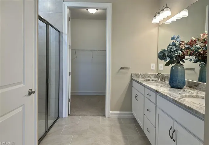 Bathroom with double vanity, light tile patterned flooring, a walk in closet, and a shower stall