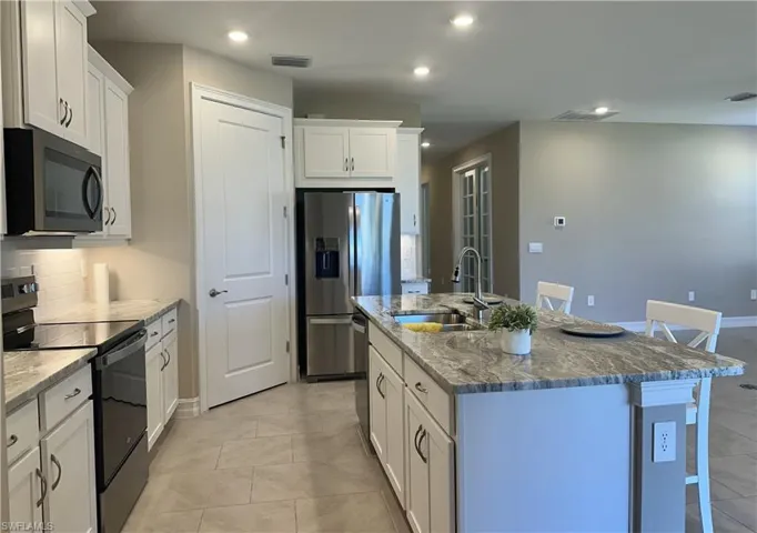 Kitchen featuring black appliances, a kitchen breakfast bar, white cabinets, light stone countertops, and recessed lighting