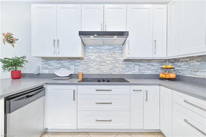 Kitchen with white cabinets, stainless steel dishwasher, dark stone counters, tasteful backsplash, and black electric stovetop