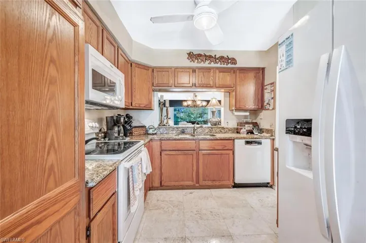 Kitchen featuring white appliances, sink, light stone counters, light tile patterned floors, and ceiling fan