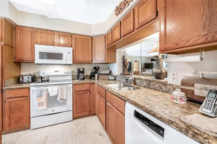 Kitchen with white appliances, light tile patterned floors, ceiling fan, light stone countertops, and sink