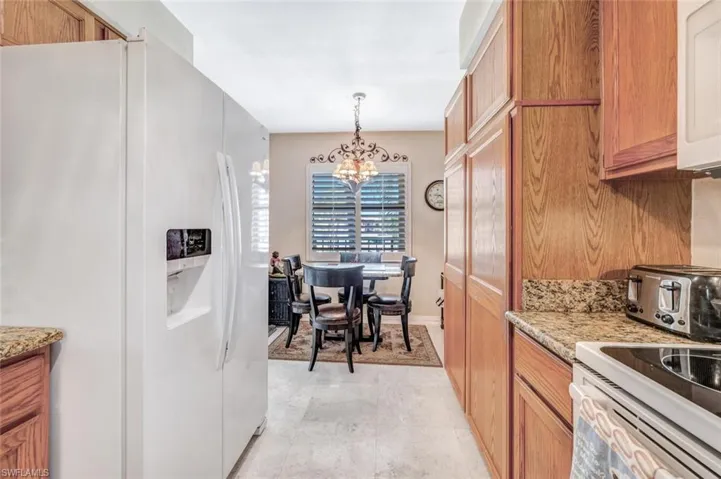 Kitchen with light tile patterned flooring, a notable chandelier, light stone countertops, white refrigerator with ice dispenser, and decorative light fixtures