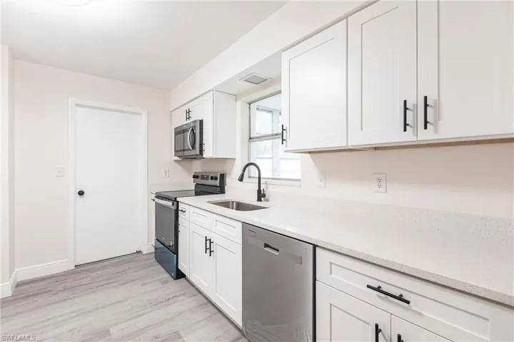 Kitchen featuring stainless steel appliances, light wood-style floors, white cabinetry, and light stone counters