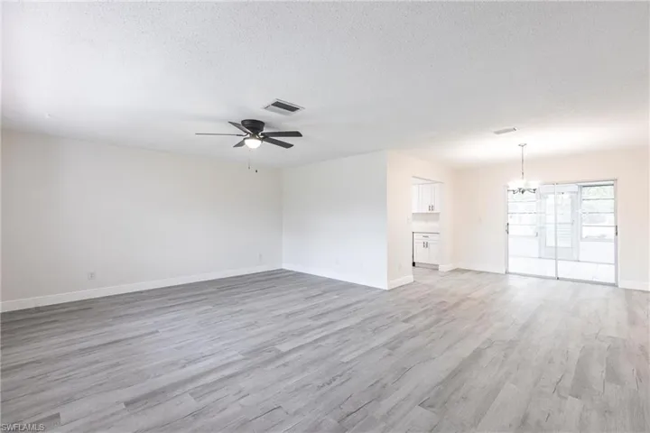 Unfurnished room with a chandelier, ceiling fan, light wood-style flooring, and a textured ceiling