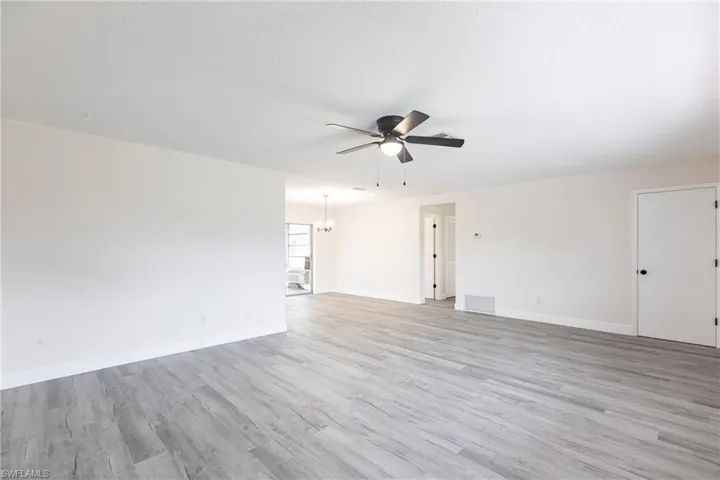 Unfurnished living room featuring ceiling fan, light wood-style floors, and a chandelier