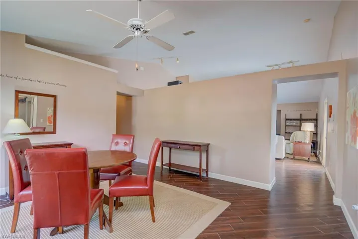 Dining room with dark wood-style floors, track lighting, vaulted ceiling, and baseboards