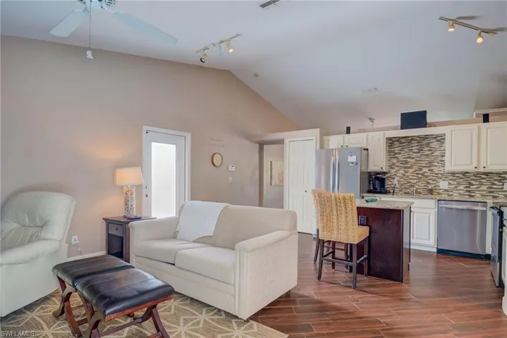 Living area featuring dark wood-style floors, track lighting, ceiling fan, and lofted ceiling