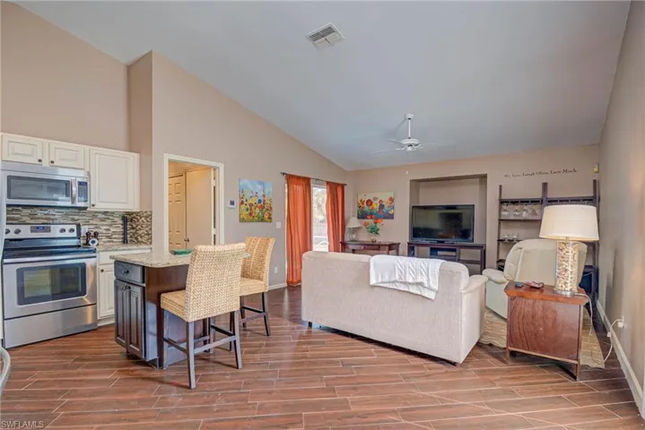 Living room with wood finished floors, baseboards, visible vents, a ceiling fan, and high vaulted ceiling