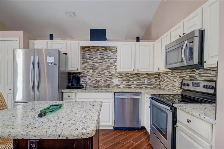 Kitchen with light stone counters, visible vents, stainless steel appliances, dark wood-style flooring, and backsplash