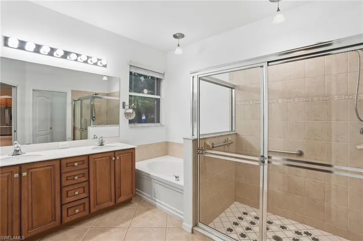 Primary bathroom featuring double vanity, a bath, a stall shower, and light tile patterned floors