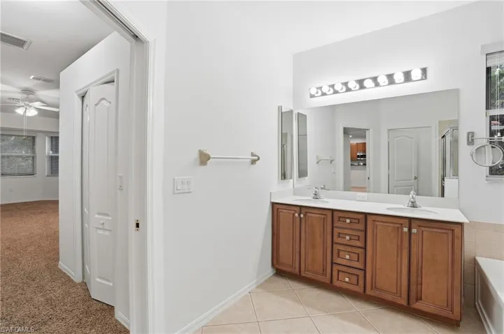 Primary bathroom featuring double vanity, ceiling fan, a bath, a shower with shower door, and light tile patterned floors