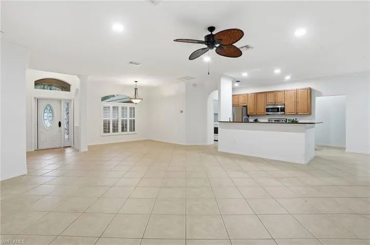 Unfurnished living room with a ceiling fan, recessed lighting, light tile patterned flooring, crown molding, and arched walkways