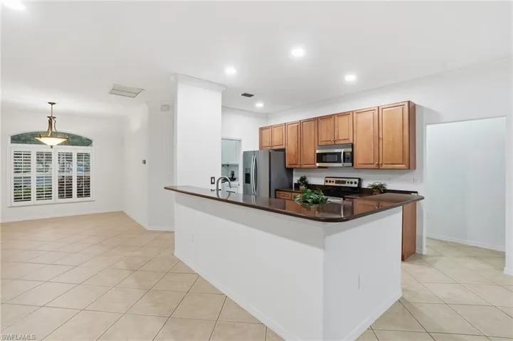 Kitchen with wood finish cabinetry, stainless steel appliances, crown molding, dark stone counters, and recessed lighting