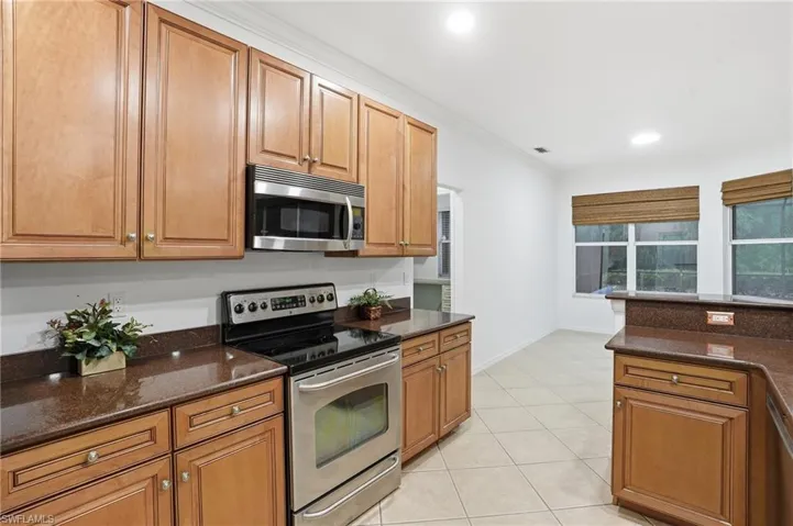 Kitchen featuring stainless steel appliances, wood finish cabinets, dark stone counters, crown molding, and light tile patterned flooring