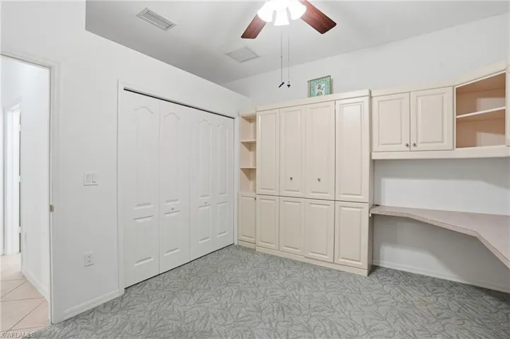 Bedroom 2 with built-in cabinets and Murphy bed, ceiling fan, and light colored carpet