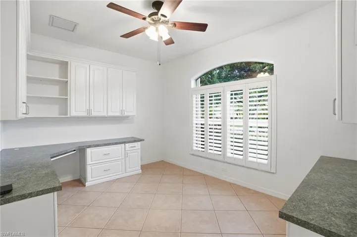 Office with built in desk, ceiling fan, and light tile patterned flooring