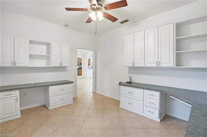 Office with built in desk, ceiling fan, and light tile patterned floors