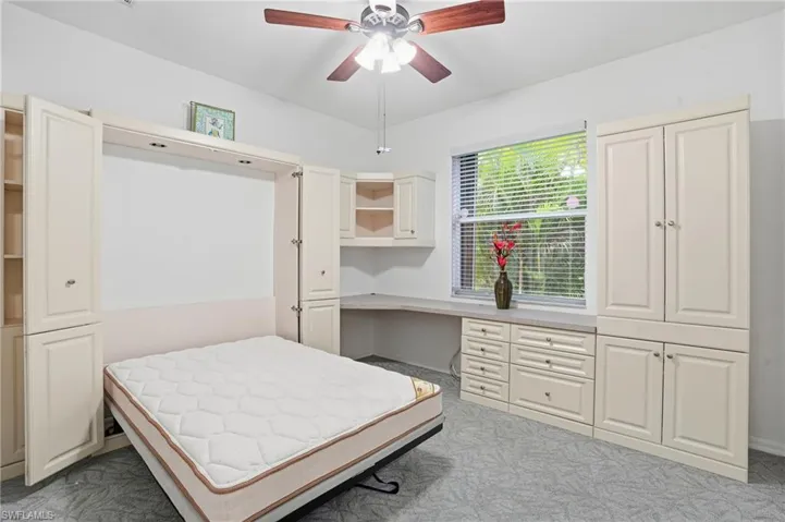 Bedroom 2 with built-in cabinets and Murphy bed, ceiling fan, and light colored carpet