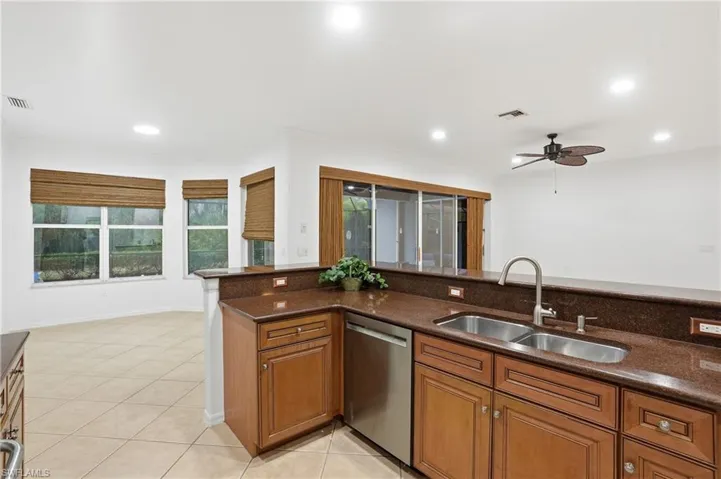 Kitchen with wood finish cabinetry, stainless steel dishwasher, dark stone counters, ceiling fan, and light tile patterned floors