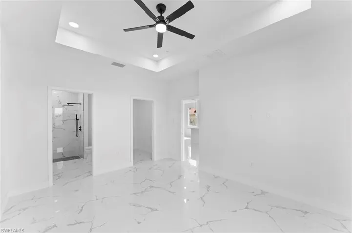Empty room featuring a raised ceiling, light tile patterned floors, and ceiling fan