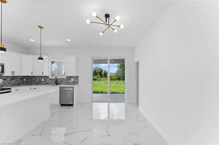 Kitchen with light tile patterned flooring, backsplash, stainless steel appliances, and decorative light fixtures