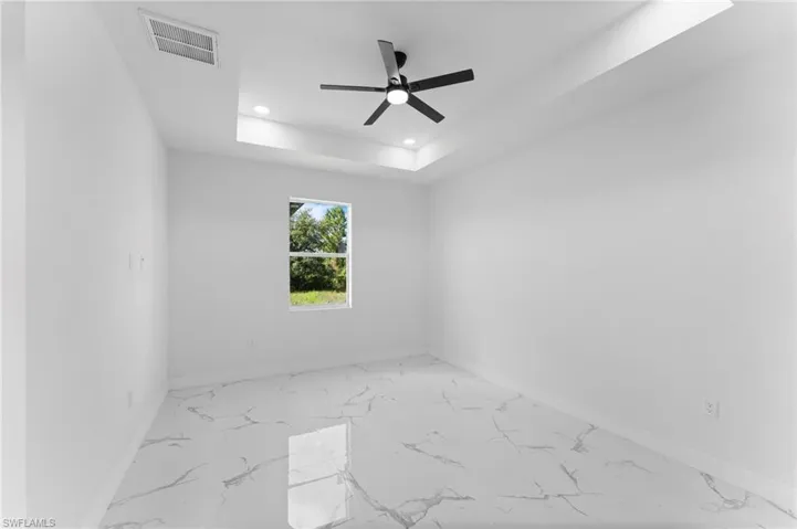 Empty room featuring ceiling fan, light tile patterned floors, and a tray ceiling