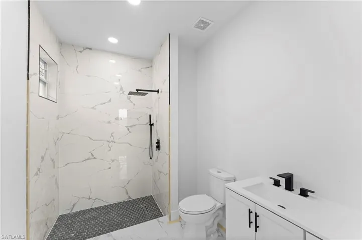 Bathroom with tile patterned flooring, toilet, vanity, and a tile shower
