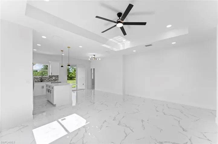 Unfurnished living room featuring light tile patterned flooring, a raised ceiling, sink, and ceiling fan
