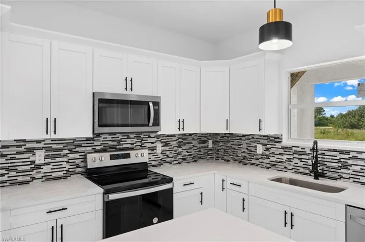 Kitchen featuring decorative light fixtures, white cabinets, tasteful backsplash, and stainless steel appliances
