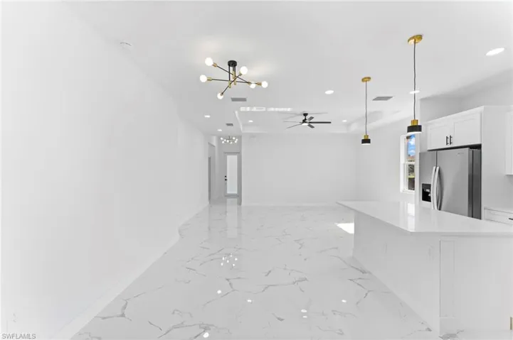 Kitchen with pendant lighting, light tile patterned floors, ceiling fan with notable chandelier, stainless steel fridge with ice dispenser, and white cabinetry