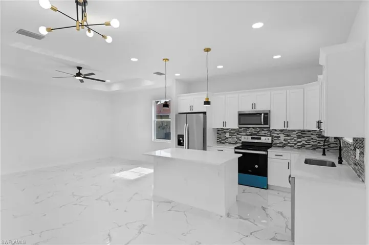 Kitchen featuring stainless steel appliances, sink, a kitchen island, decorative backsplash, and ceiling fan with notable chandelier