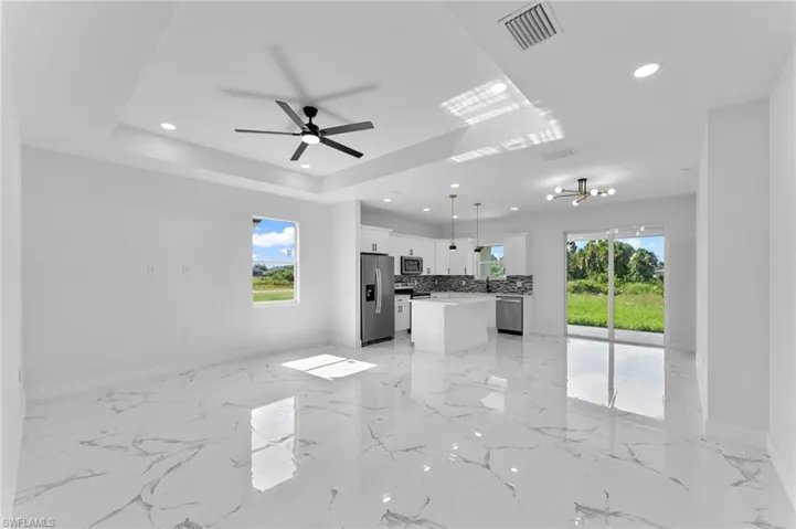 Unfurnished living room featuring ceiling fan with notable chandelier, a tray ceiling, light tile patterned floors, and plenty of natural light