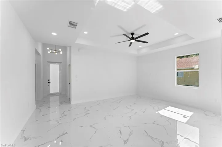 Unfurnished room with ceiling fan with notable chandelier, light tile patterned floors, and a tray ceiling