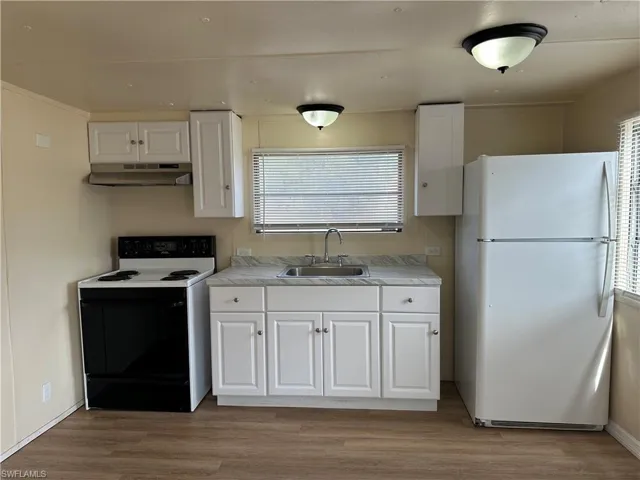 Kitchen with freestanding refrigerator, range with electric stovetop, white cabinets, and light countertops