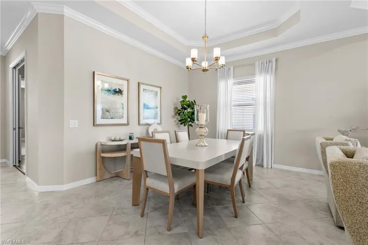 Dining area with light tile patterned floors, baseboards, ornamental molding, a chandelier, and a tray ceiling