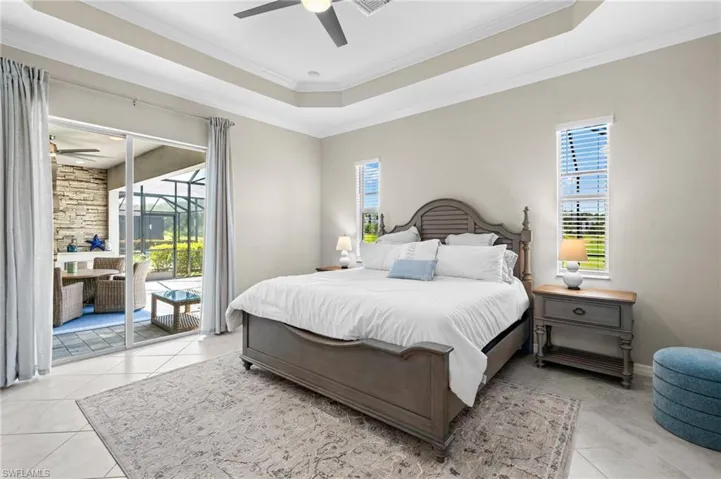 Bedroom featuring light tile patterned floors, ornamental molding, ceiling fan, a tray ceiling, and access to exterior