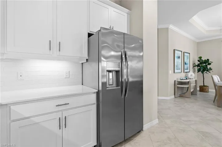 Kitchen with stainless steel fridge with ice dispenser, ornamental molding, light countertops, white cabinetry, and decorative backsplash