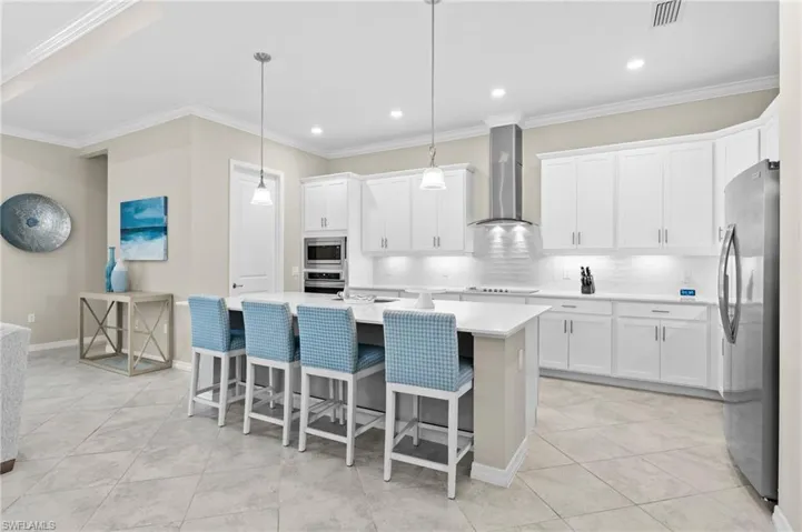 Kitchen featuring visible vents, wall chimney range hood, light countertops, appliances with stainless steel finishes, and white cabinetry