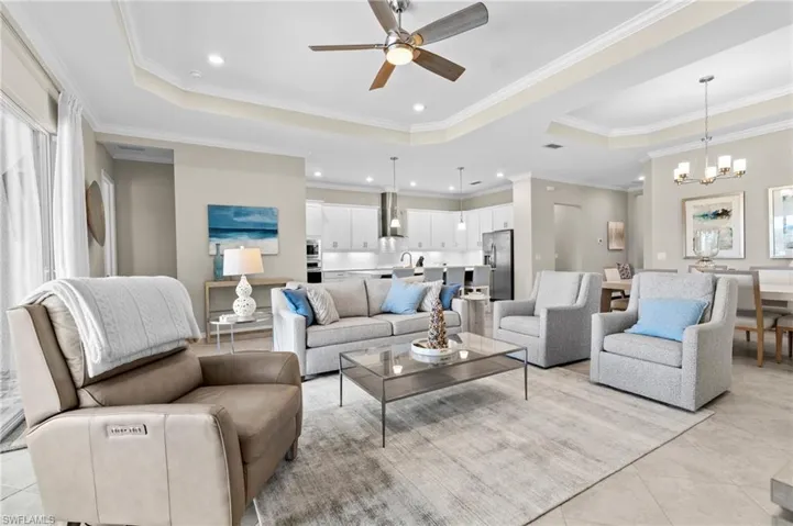 Living area with ceiling fan with notable chandelier, light tile patterned floors, ornamental molding, recessed lighting, and a raised ceiling