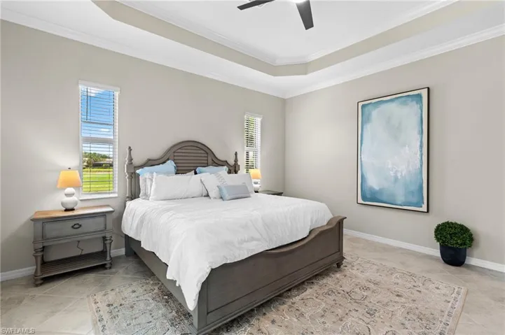 Bedroom featuring crown molding, light tile patterned floors, ceiling fan, a raised ceiling, and baseboards