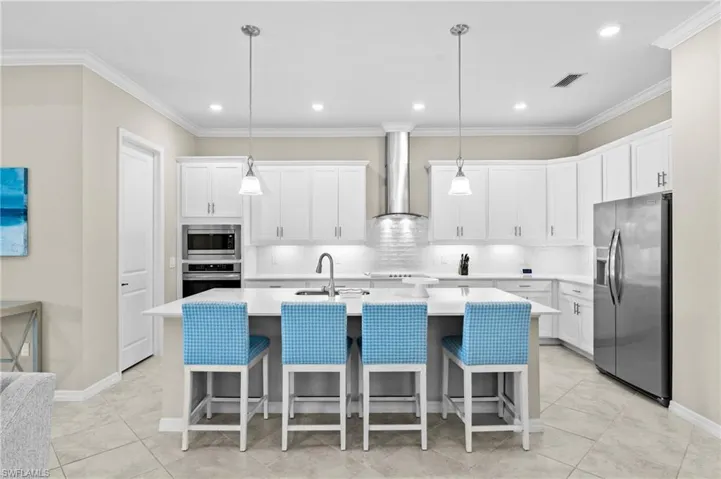 Kitchen featuring wall chimney exhaust hood, tasteful backsplash, appliances with stainless steel finishes, a kitchen island with sink, and light countertops