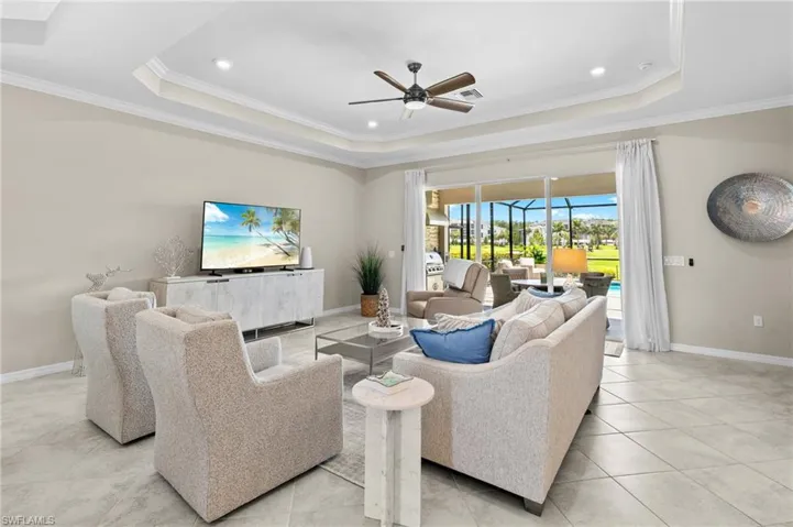Living area featuring ceiling fan, ornamental molding, visible vents, a raised ceiling, and baseboards