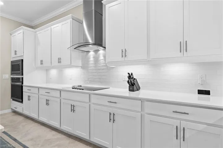 Kitchen featuring wall chimney exhaust hood, light countertops, appliances with stainless steel finishes, crown molding, and white cabinetry