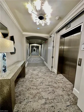 Corridor with crown molding, carpet flooring, an inviting chandelier, and elevator