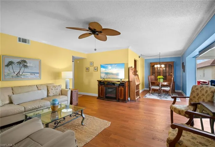 Living area with a textured ceiling, wood finished floors, ornamental molding, a chandelier, and a ceiling fan