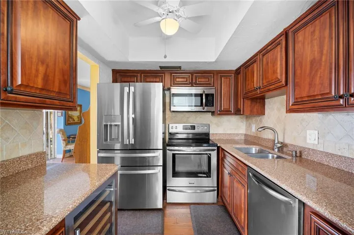 Kitchen with tasteful backsplash, stainless steel appliances, light stone countertops, beverage cooler, and a raised ceiling